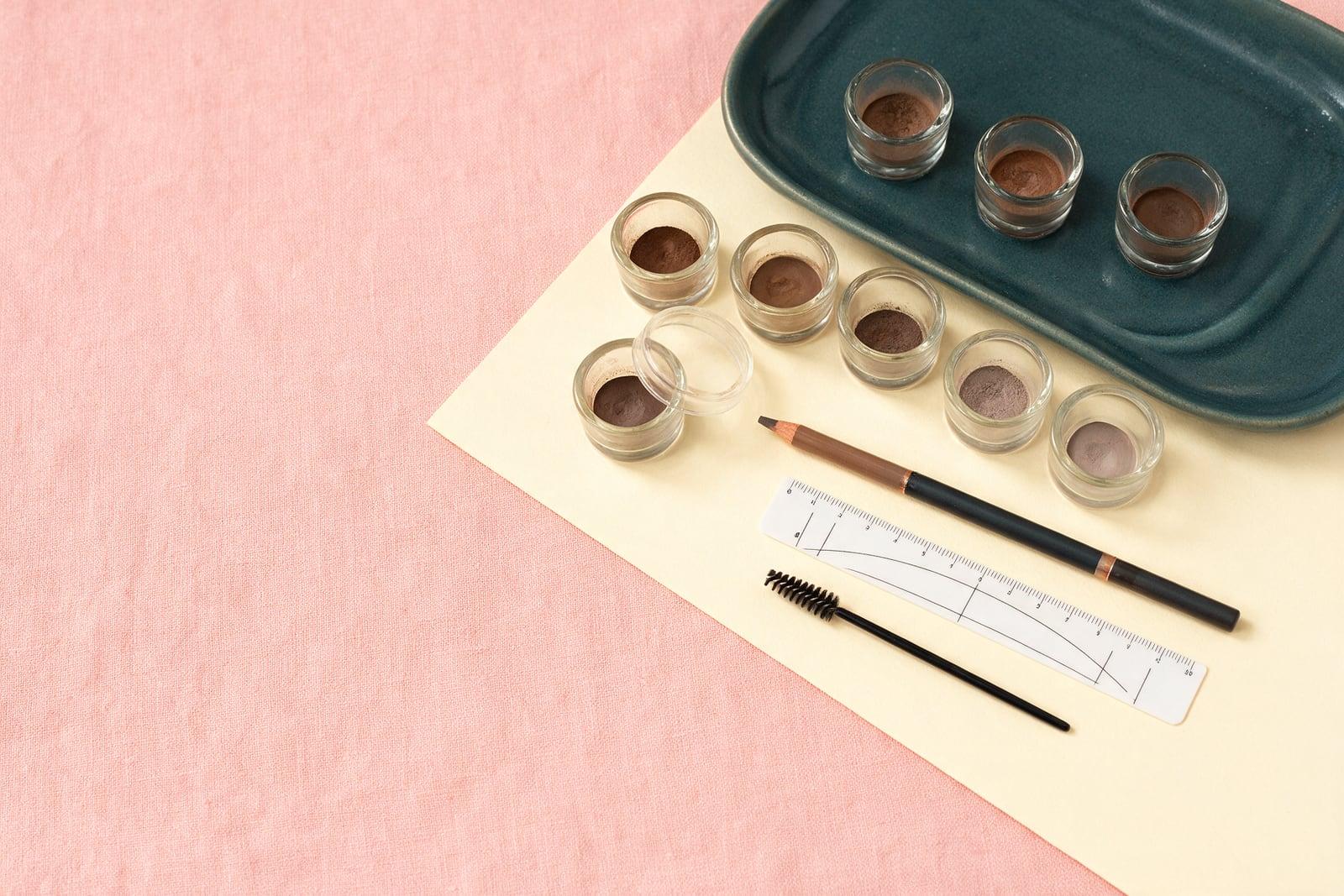 Brow pigments, pencil and mapping ruler on pink linen